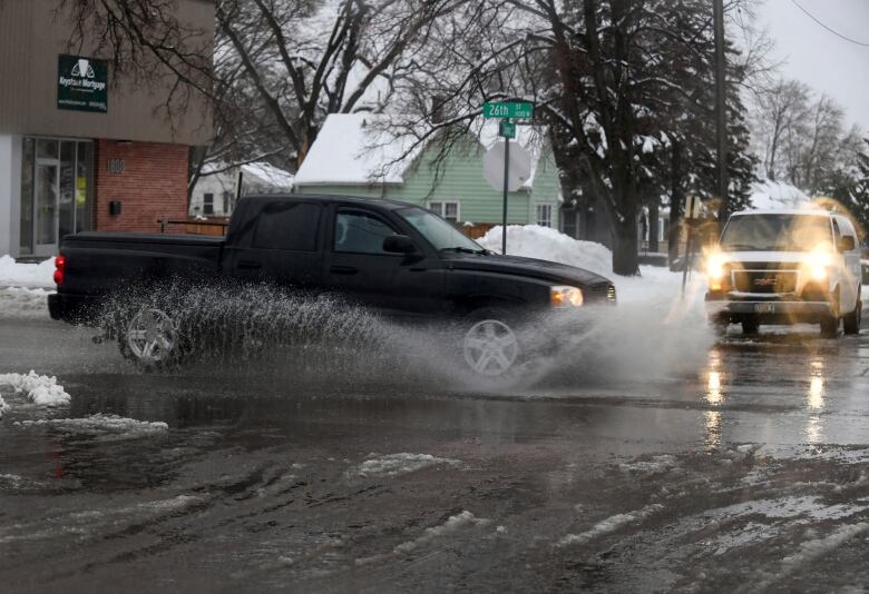 A pickup truck drives through a slushy intersection, sending up a large wave.