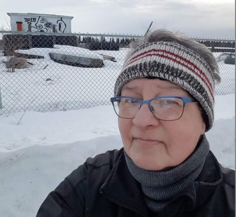 A woman in a knitted headband looks at the camera, there is a snowy background.