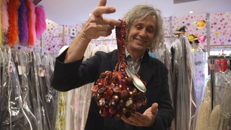 Simon Lugassy, co-owner of Original, a store on Queen West holds a colourful purse up to the camera while smiling largely.