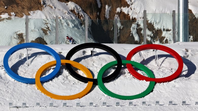 A large display of the Olympic rings is propped up on the side of a snowbank, in front of a snow-covered mountain base.