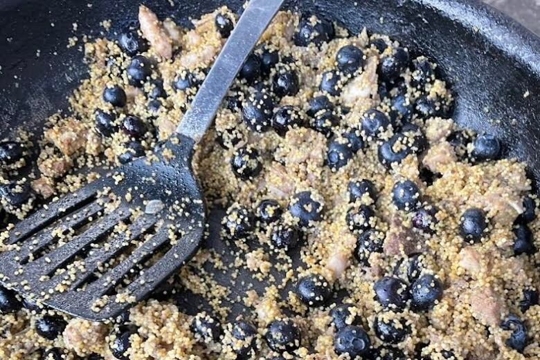 Inside a frying pan is a spatula and a mixture of blueberries and small fish eggs.