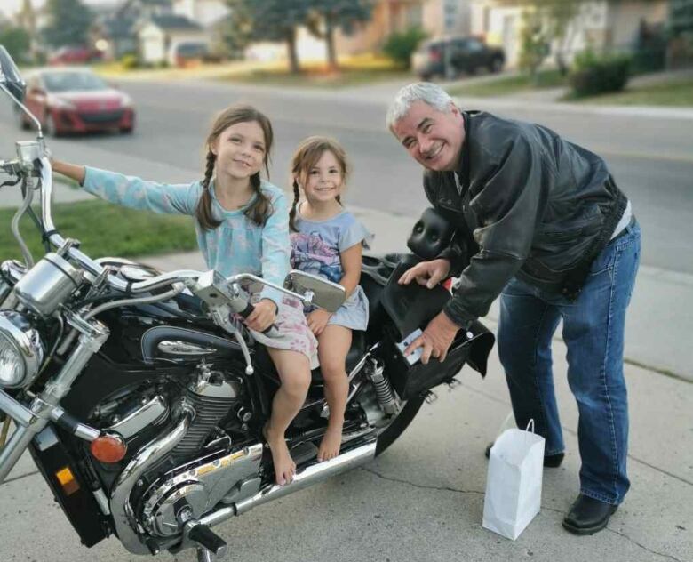 Two girls sit on a motorbike while a man holds it steady.