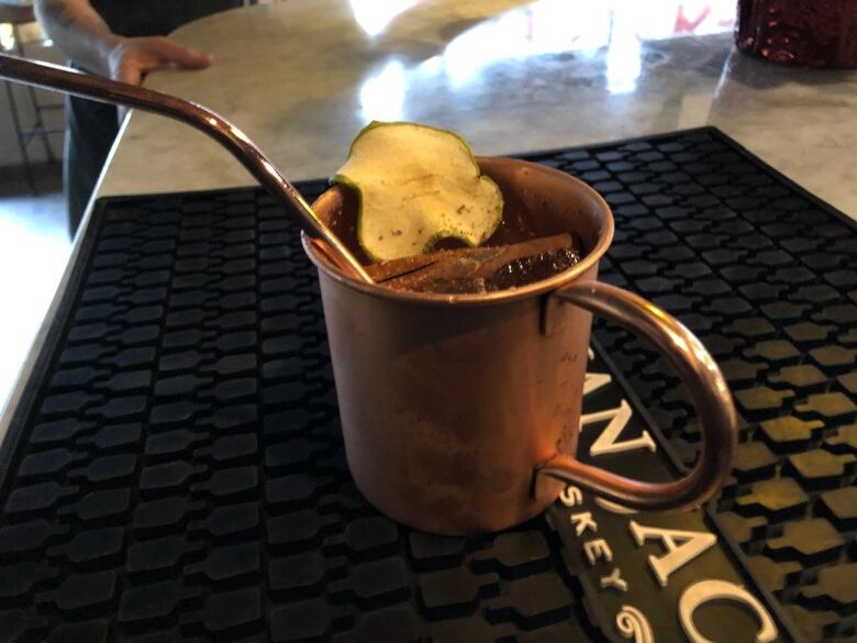 A copper mug with a matching copper straw with spices and a dried apple slice on top. 