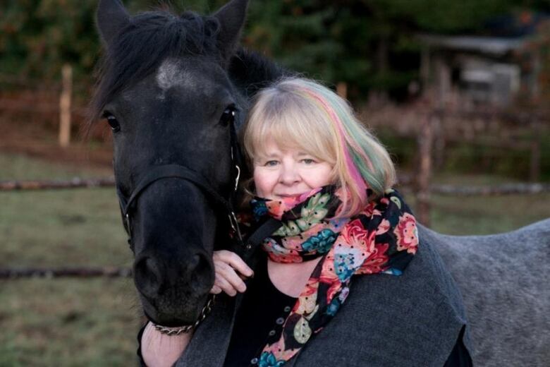 A woman wearing a colourful sweater hugs a black horse.