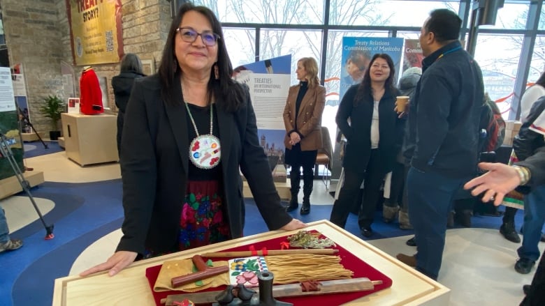 A woman with long dark hair stands behind a table, on which is a traditional First Nations pipe.