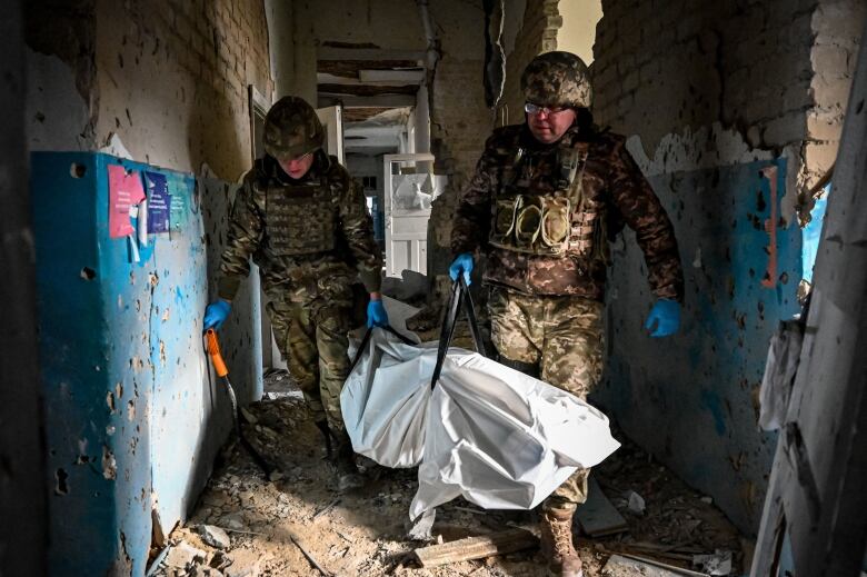 Ukrainian servicemen carry a plastic bag containing the body of a killed Russian soldier found in a destroyed hospital building of the liberated village of Petropavlivka near Kupiansk, Kharkiv region on December 15, 2022,