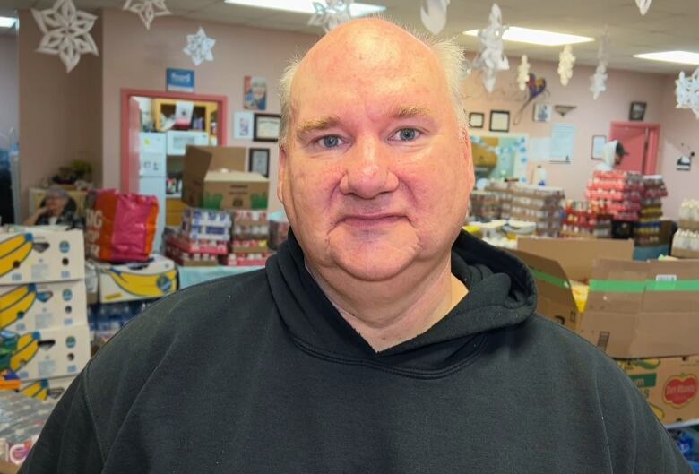 A man in a black shirt stands in front of a room full of donated food. 