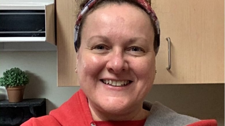 A woman stands in a kitchen, smiling at the camera.