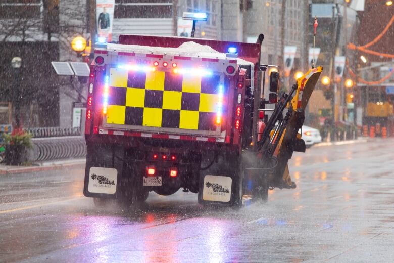 A snow vehicle can be seen driven down a street as wet snow falls.