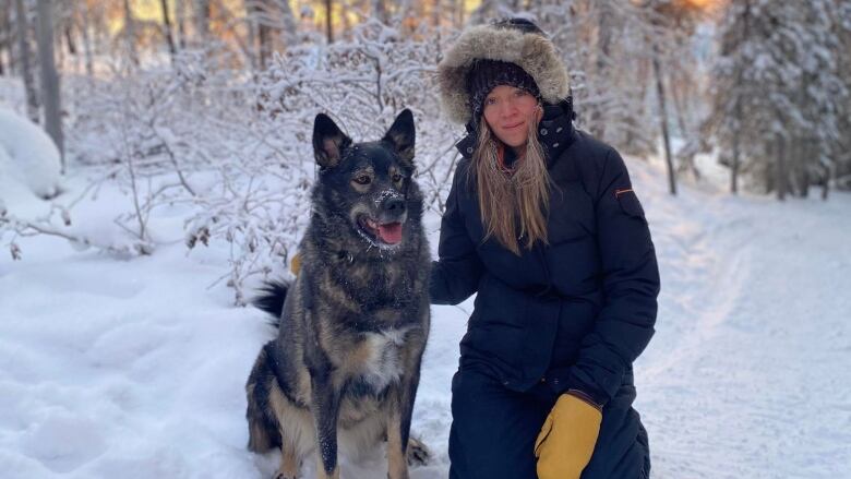 A woman stands in the snow beside her pet dog.