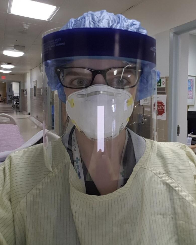 A registered nurse faces the camera wearing a mask and face shield