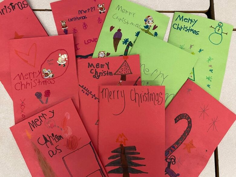 A pile of cards on red and green craft paper with childrens' drawings on the front.