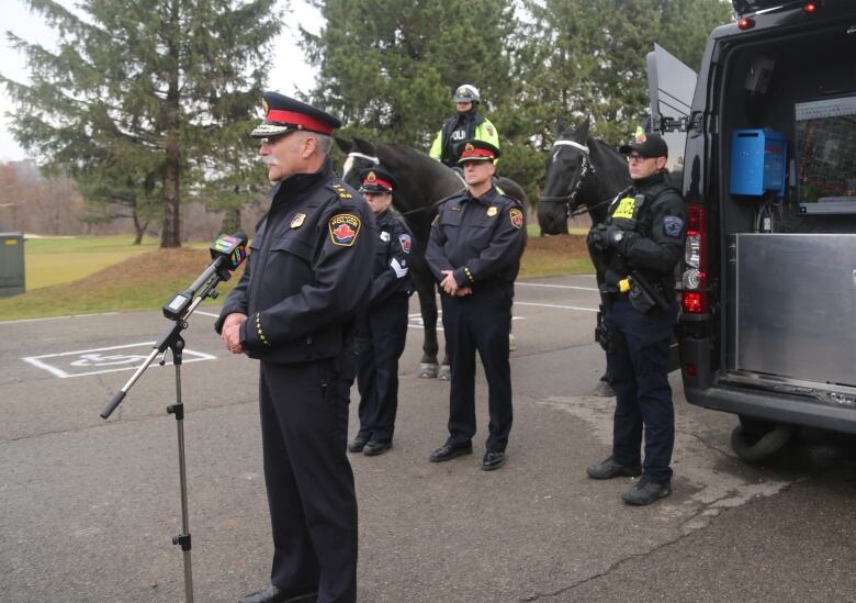 Police officers and police horse gather around during a press conference. 