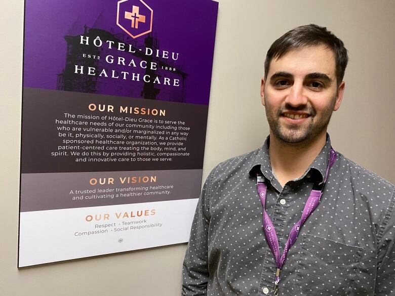 Kevin Matte stands next to a Hotel-Dieu Grace Healthcare sign, mounted to a wall, that explains the organization's mission, vision and values.