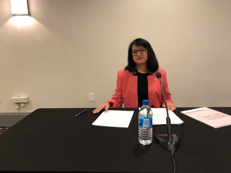 Manju Varma sits at a table with papers and a microphone in front of her.