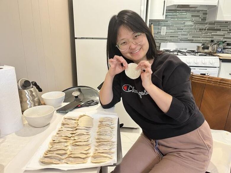 girl with glasses, sitting down, smiling, holding uncooked dumpling