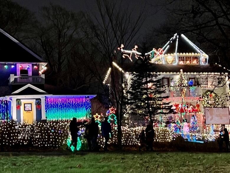 Silhouettes walk past houses that are festooned with Christmas lights.