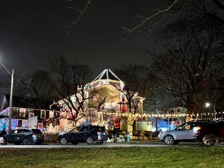 Cars driving by home covered with lights and Christmas ornaments