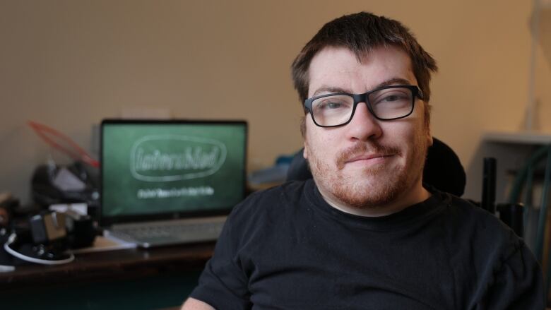 A man with a beard and glasses in a wheelchair looks at the camera.