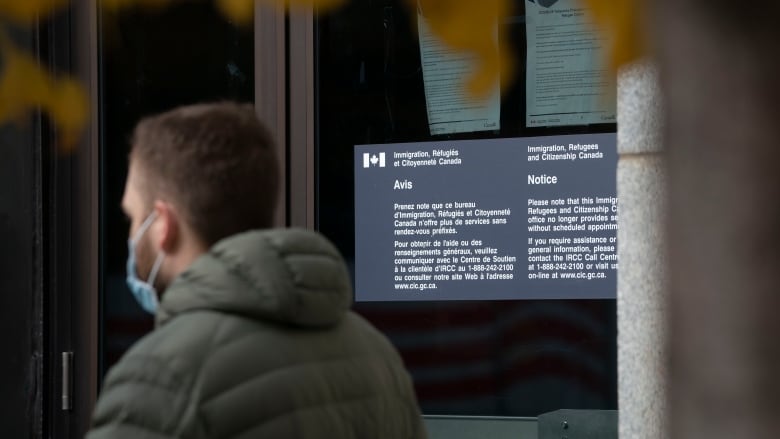  A man in a mask walks by a building with 'Immigration, Refugees, Citizenship Canada' written on a sign.