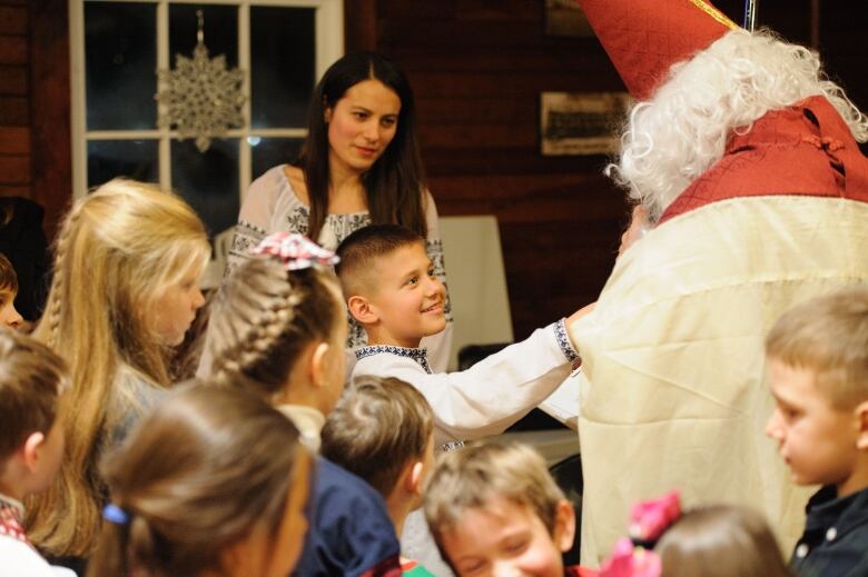 A woman and her son dressed in Ukrainian outfits meet St. Nicholas, who is dressed in red with a white beard. 