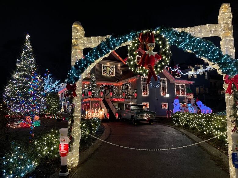 House with chocolate brown siding is brightly illuminated with multicoloured Christmas lights. A tree in the foreground is also illuminated with blue and green lights