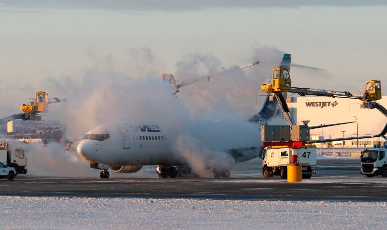 Clouds of steam rise from a white airplane positioned on a runway marked with snow. 