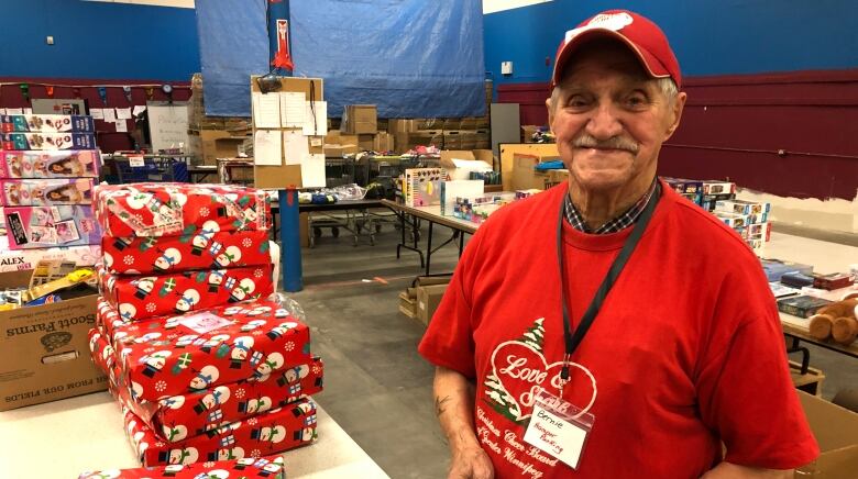 A man stands beside a tower of Christmas present he wrapped.