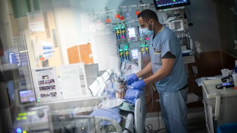 A nurse at an ICU in B.C. checks on a patient in a hospital bed at Royal Columbian Hospital.