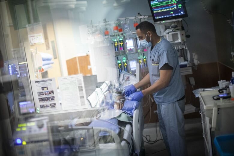 A nurse at an ICU in B.C. checks on a patient in a hospital bed at Royal Columbian Hospital.