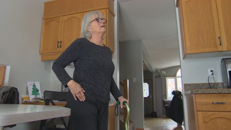 A woman who is standing has one hand rested on her hip and the other hand on her cane.