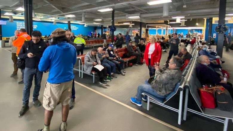 A crowd of people are standing and sitting in an airport terminal.