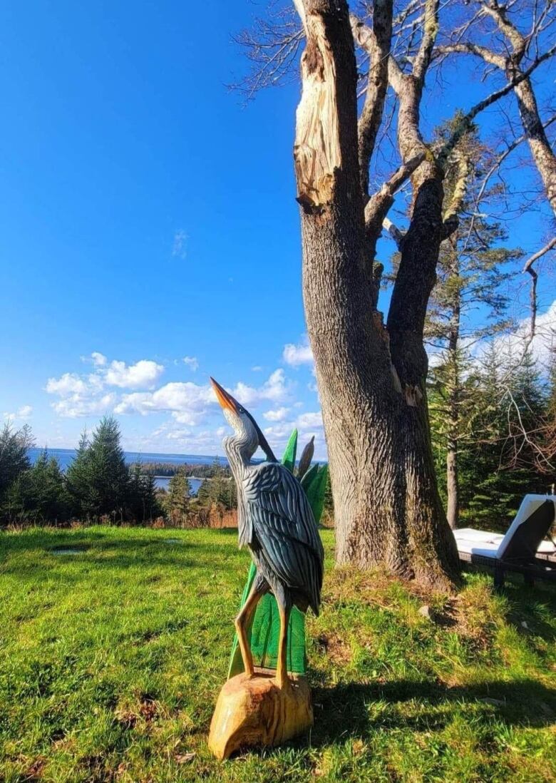 A wooden heron stands in front of a maple tree. 