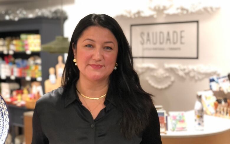 A woman with dark hair and wearing a black shirt poses for a portrait in a small store.