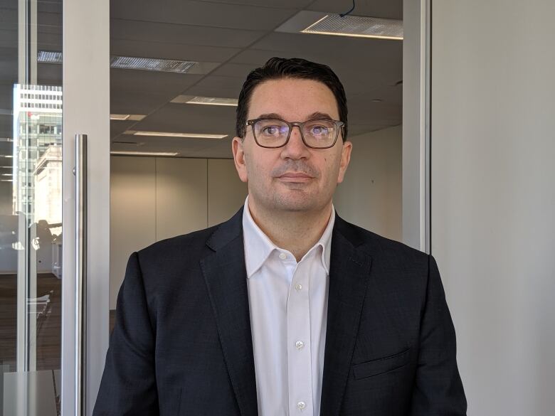 A man wearing glasses and a suit jacket poses for a portrait in an office.