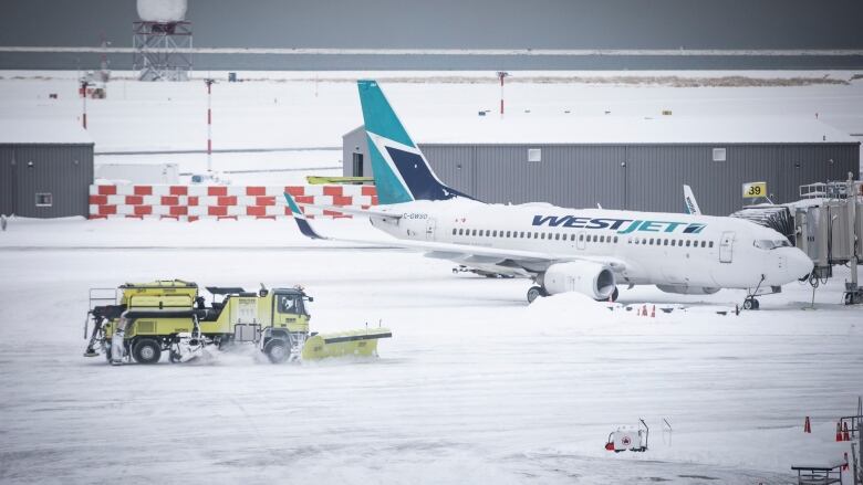 A lime green snow plow clears snow off the tarmac at Vancouver International Airport. A WestJet plane is seen in the background.