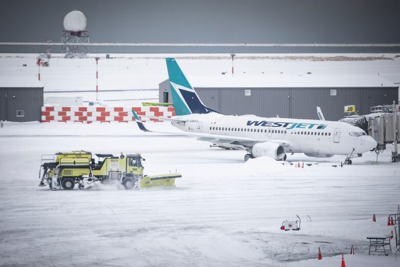 A lime green snow plow clears snow off the tarmac at Vancouver International Airport. A WestJet plane is seen in the background.