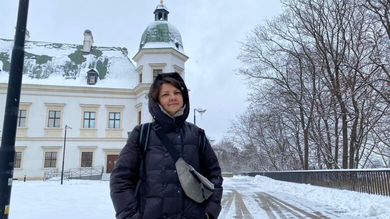 A woman in a parka stands in front of a building