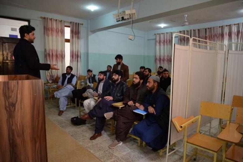 Men attend a university class in Afghanistan, while chairs for female students sit empty.