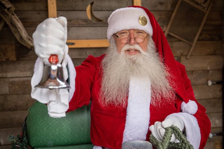 A man dressed as Santa Claus rings a bell while sitting in a sleigh. 