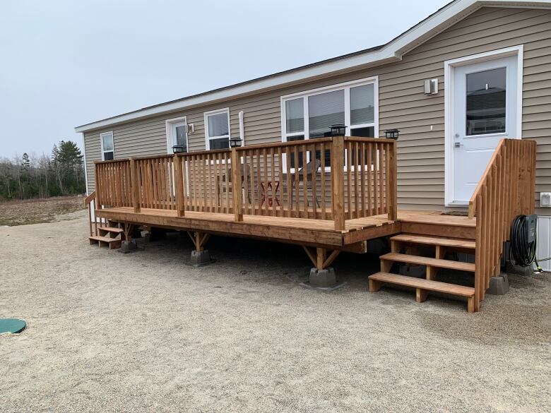 A beige mobile home with a wooden patio surrounded by a railing.