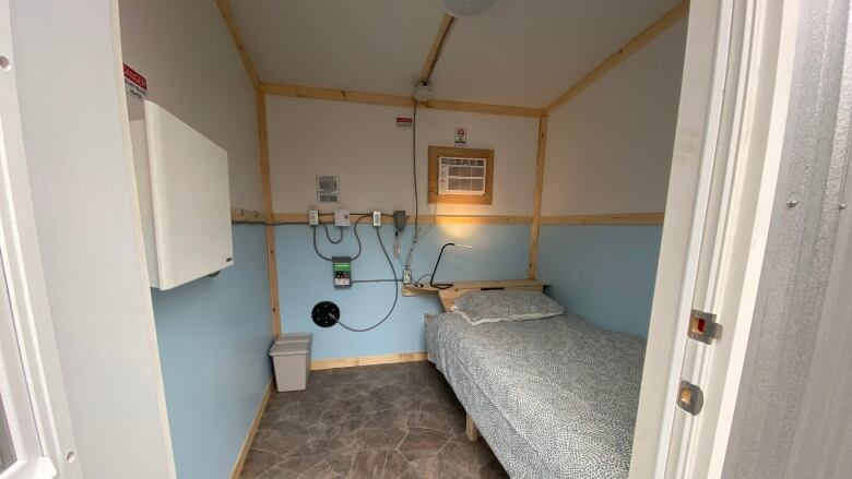 A small room with blue walls, laminate flooring and a single bed with a lamp.