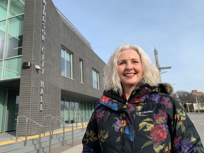 A woman with white hair wearing a black jacket with flowers on it standing in front of Windsor City Hall