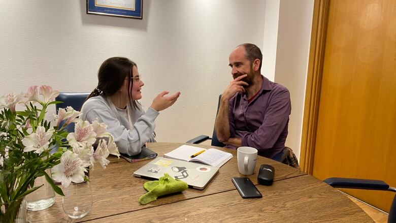 A woman and a man are sitting at a desk having a conversation.