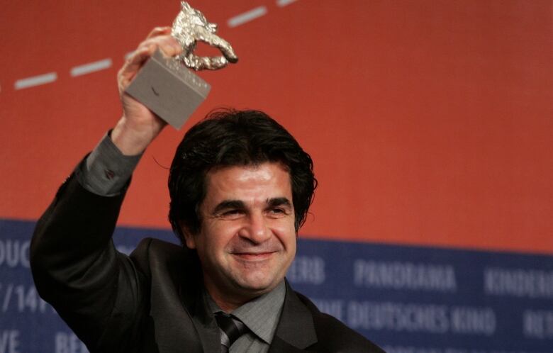 A man wearing a suit poses with a silver bear statue in front of a red backdrop.