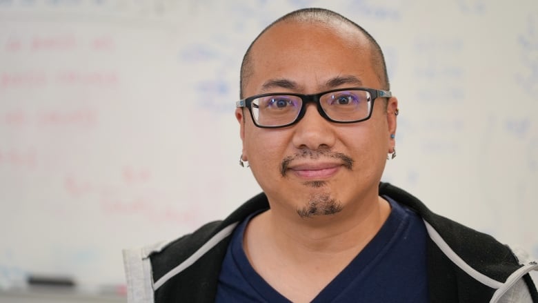 Man with glasses, small goatee and one ear piercing in each ear.