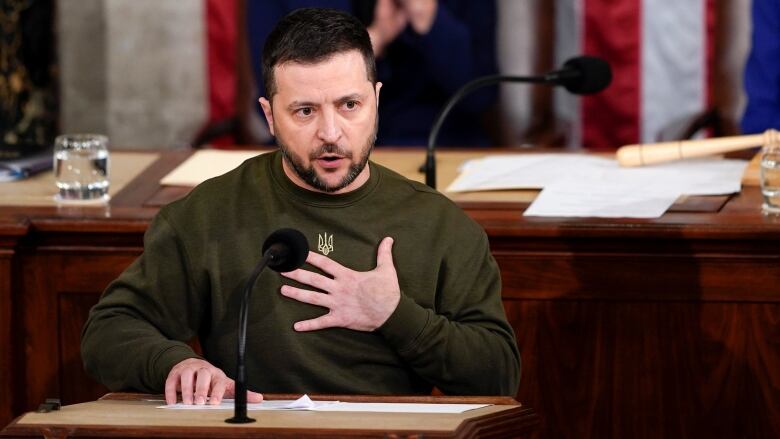 A man in a green military sweater delivers a speech.