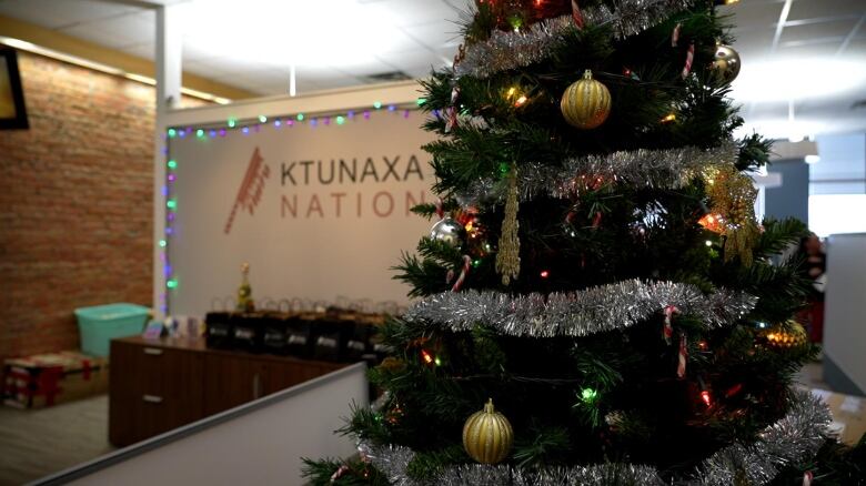 A Christmas tree in front of a wall written with words 