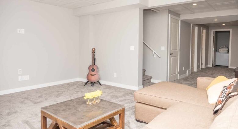 The living room in a basement suite with Calgary. It's equipped with a beige couch, a coffee table and a guitar in the corner.