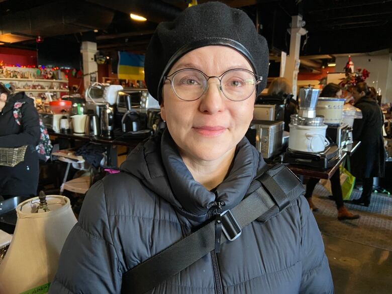 A woman stands in a room filled with donated objects such as microwaves, coffee pots, lamps and Christmas decorations.